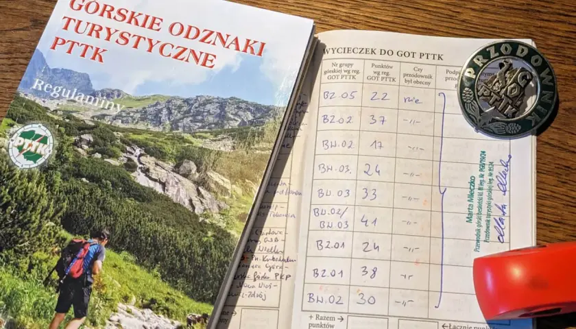 Książeczka GOT PTTK z wpisami wycieczek i odznaką przodownika.