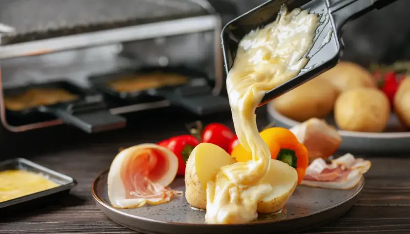 Formaggio fuso in padella, filante e dorato, viene versato su patate e salumi. Un piatto invitante e gustoso.