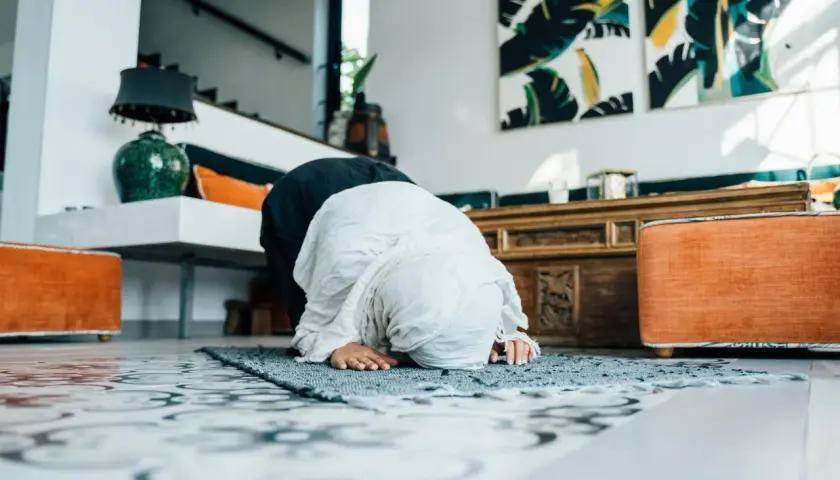 Kobieta w hidżabie wykonuje modlitwę codzienną na dywaniku w przestronnym, nowoczesnym wnętrzu.