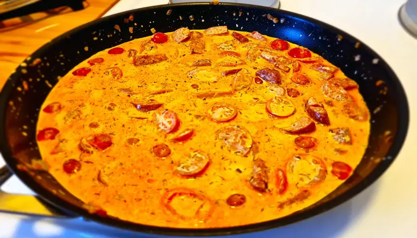 En krämig korv stroganoff deluxe i en stekpanna, med skivad korv och körsbärstomater i en gyllene sås.