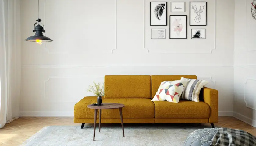 Ein gemütliches kleines Wohnzimmer einrichten mit einem senfgelben Sofa, Kissen, einem Beistelltisch und Wandkunst.