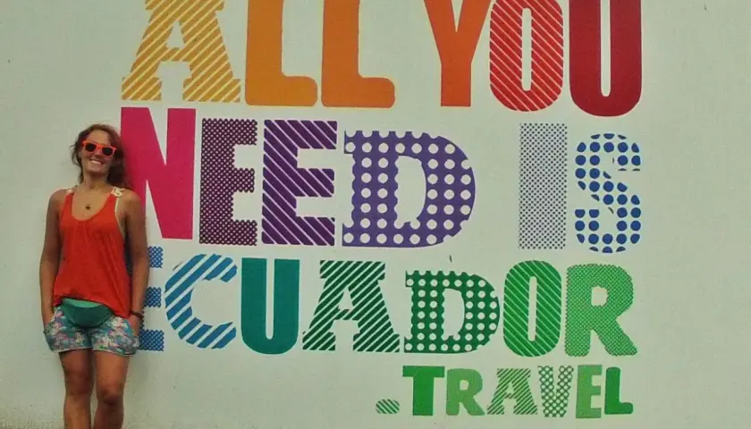 Uśmiechnięta turystka w Vilcabamba pozuje na tle kolorowego napisu "All you need is Ecuador. Travel".