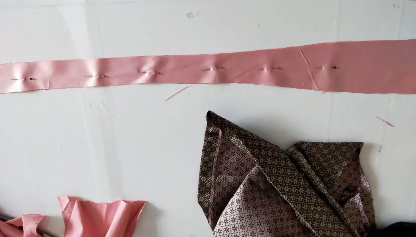 Różowa taśma z agrafkami, przygotowana do poszerzenia sukienki po bokach. Obok leży wzorzysta tkanina.