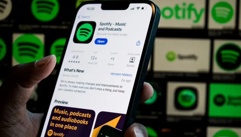 Dłoń trzyma smartfon z otwartą aplikacją Spotify. W tle widać ikony Spotify.
