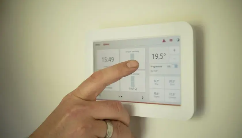 Dłoń dotyka ekranu termostatu, który pokazuje temperaturę 19,5°C. To nowoczesne rozwiązanie, które może być częścią systemu z piecem kondensacyjnym.