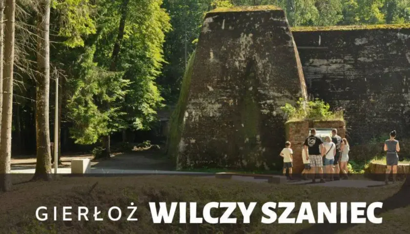 Grupa turystów zwiedza historyczny Wilczy Szaniec w Gierłoży, podziwiając potężne bunkry w otoczeniu zieleni.