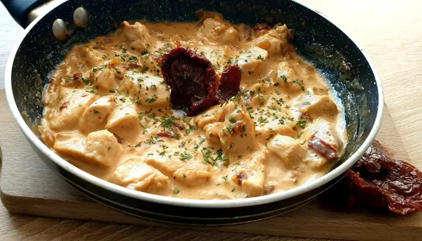 Kawałki kurczaka w kremowym sosie z suszonymi pomidorami i natką pietruszki. Danie "marry me chicken" wygląda apetycznie.