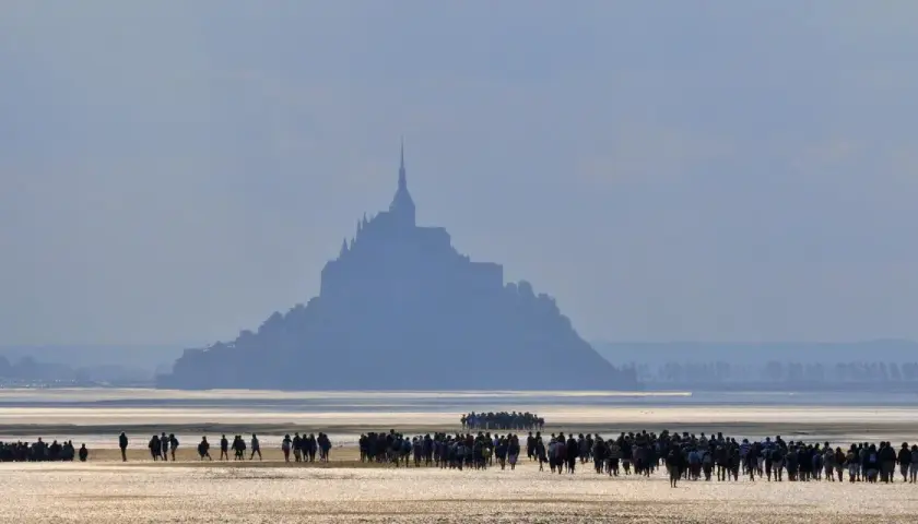 Silhouetten von Menschen auf dem Wattboden, die sich dem majestätischen Mont Saint-Michel nähern.