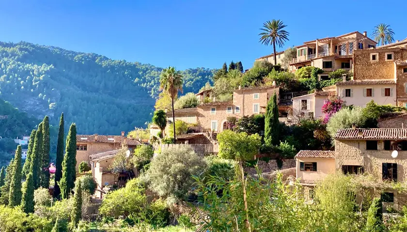Malerische Steinhäuser schmiegen sich an einen grünen Hang. Palmen und Zypressen wachsen zwischen den Gebäuden. Ein friedlicher Anblick von Mallorca im Dezember.