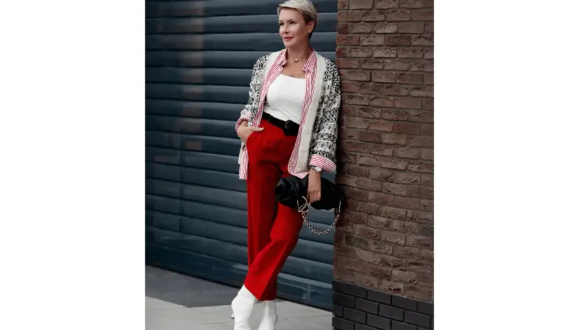 Elegancka kobieta w czerwonych spodniach i wzorzystej marynarce, z czarną torebką na łańcuszku. Stylowe czerwone spodnie stylizacje.
