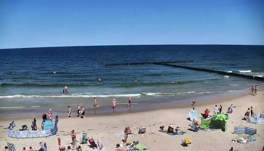 Słoneczna plaża w Dźwirzynie, ludzie kąpią się w morzu i odpoczywają na piasku. To jedne z wielu atrakcji tego miejsca.