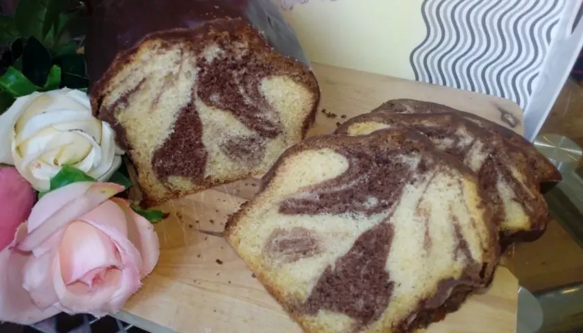 Wilgotna babka marmurkowa na oleju, oblana czekoladą, prezentuje się apetycznie obok róż.
