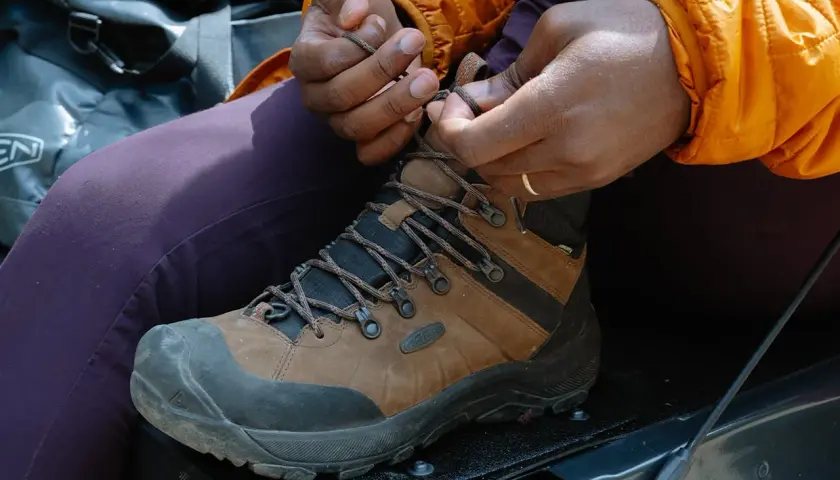 Close-up of hands tying brown hiking boots, demonstrating how to tie hiking boots for an outdoor adventure.
