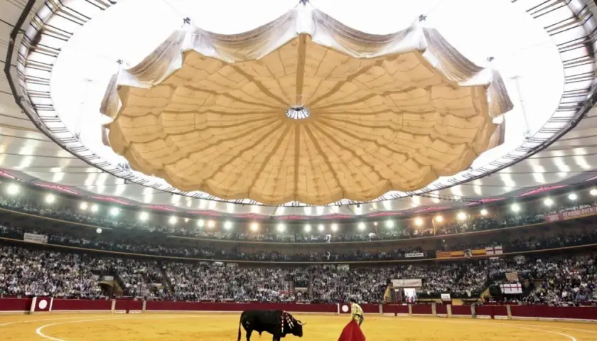 Un torero y un toro en la arena de la plaza de toros La Misericordia, con el público en las gradas y un llamativo techo desplegable.