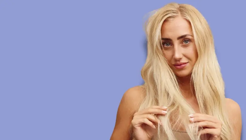 Blond kvinna med långt, tjockt hår som verkar ha hög porositet. Hon rör vid sitt hår med fingrarna.