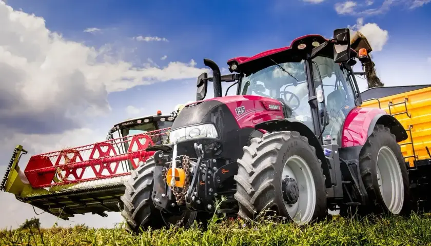 Czerwony traktor Case IH z hederem żniwnym i żółtą przyczepą. Warto wiedzieć, jak wymienić olej w takim sprzęcie, by służył latami.