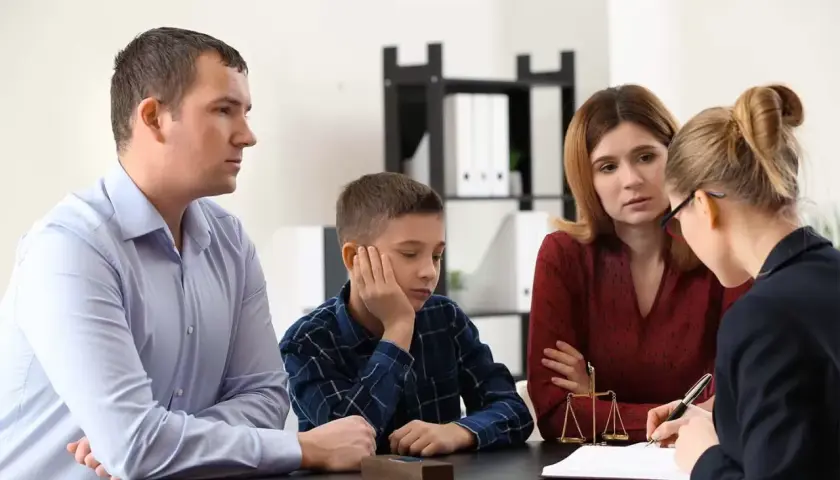 Rodzina z dzieckiem rozmawia z prawniczką przy biurku, na którym stoi waga sprawiedliwości.