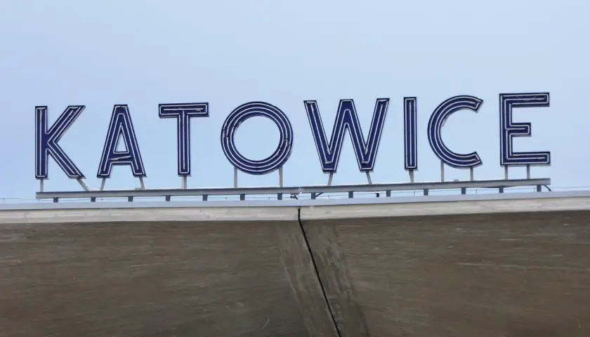 Napis "KATOWICE" z niebieskimi neonami na tle jasnego nieba.