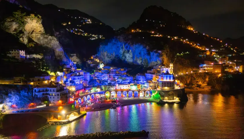 A vibrant night view of Vietri sul Mare, with buildings illuminated in colorful lights reflecting on the water.