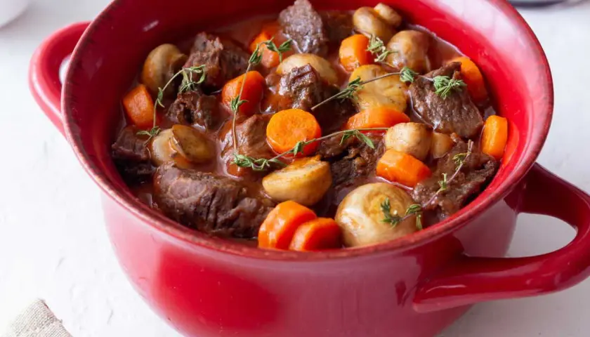 Un plat rouge rempli de bœuf bourguignon facile, avec des morceaux de bœuf tendres, des carottes et des champignons, garni de thym frais.