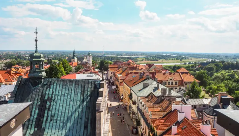 Widok z góry na urokliwy sandomierz rynek z brukowaną uliczką, kamieniczkami i kościelnymi wieżami w tle.