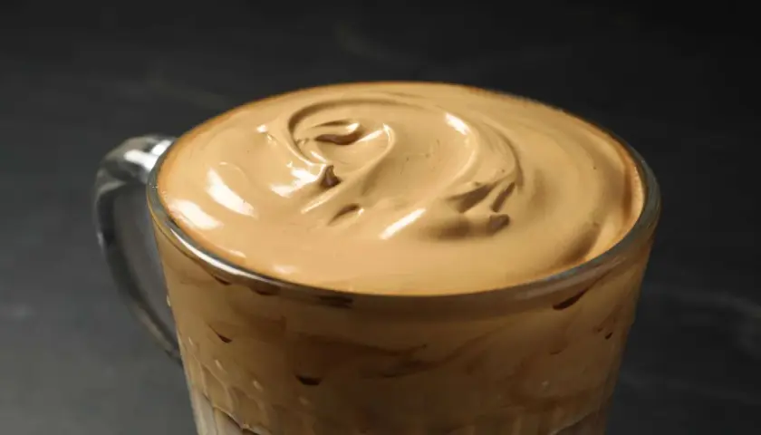 Cremiger Dalgona Kaffee in einem Glas, die aufgeschlagene Schaumkrone wirbelt wie ein Kunstwerk.