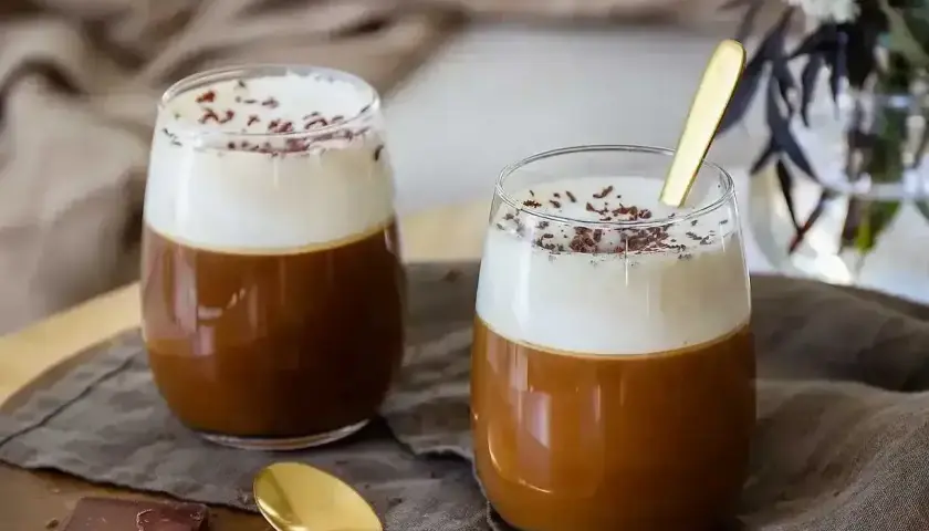 Två glas med krämig irish coffee, toppad med vispgrädde och chokladströssel. En gyllene sked vilar i det ena glaset.