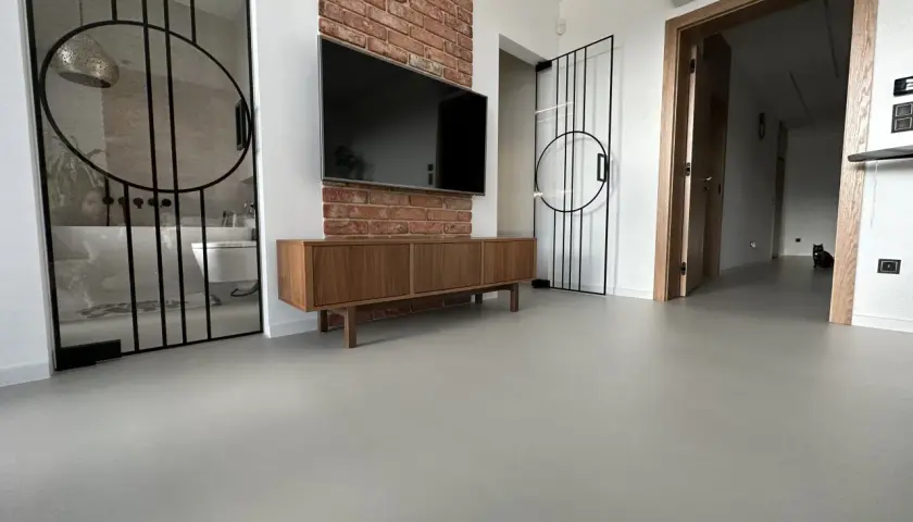 Nowoczesne wnętrze z betonową podłogą, co to jest mikrocement, która nadaje mu surowego charakteru. W tle widać łazienkę i salon.