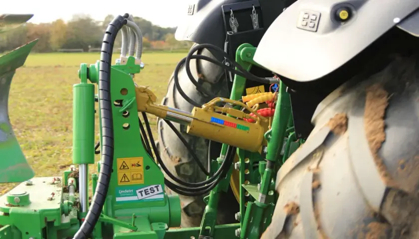 Grüner Traktor mit angehängtem Pflug. Ein gelber Walterscheid Oberlenker mit Hydraulikzylinder ist sichtbar.