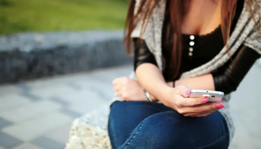 Dziewczyna z różowym lakierem na paznokciach pisze sms-a, zastanawiając się, jak wkręcić chłopaka przez sms.