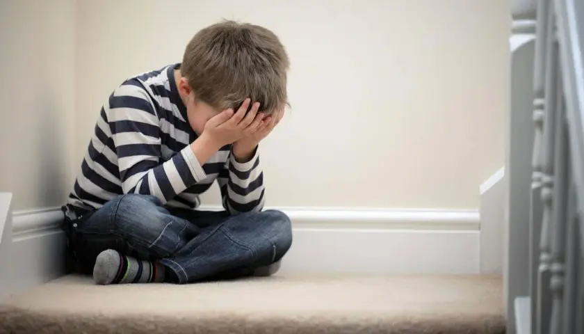 Bambino seduto sulle scale, con le mani sul viso, simbolo della delusione dei figli.