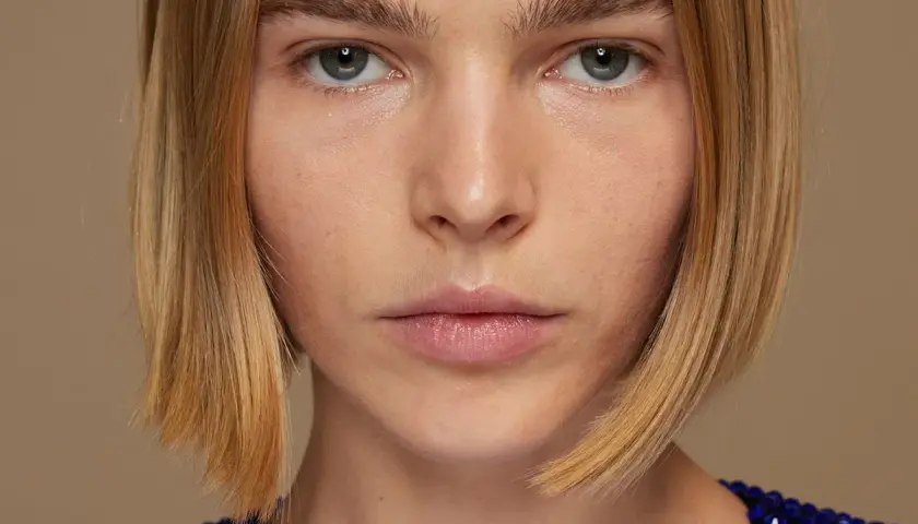 Primer plano de una mujer con un corte bob rubio y un vestido azul brillante.