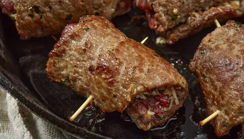 Involtini di carne succulenti, cotti in padella, con ripieno visibile e stuzzicadenti.