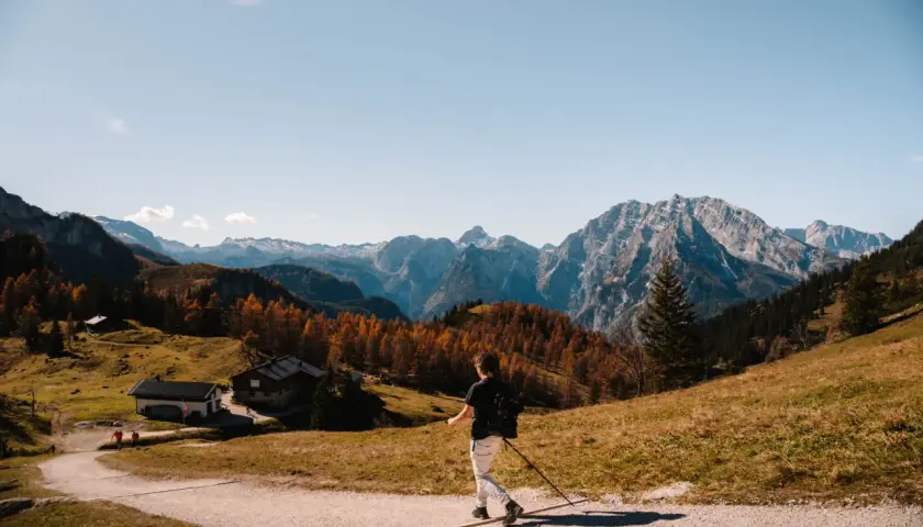 A lone hiker enjoys a scenic autumn day hiking in Bavaria, with colorful trees and majestic mountains in the background.