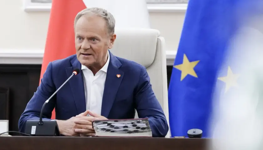 Donald Tusk w Sosnowcu, przemawia przy mikrofonie, za nim flagi Polski i UE.