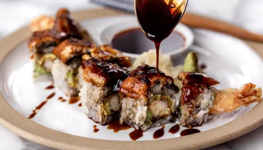 A spoon drizzles rich unagi sauce over a delicious sushi roll, showcasing how to make unagi sauce for a perfect finish.