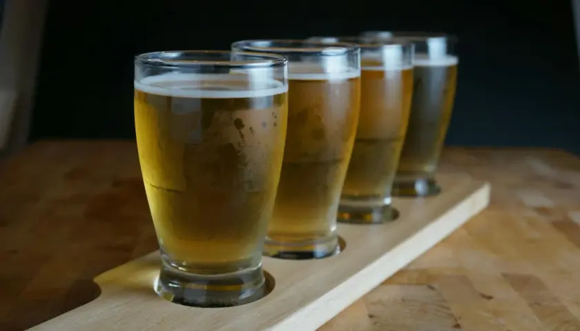 Degustacja piwa rzemieślniczego: cztery schłodzone piwa w szklankach na drewnianej desce. Poznaj zasady serwowania piwa: temperatura i szkło.