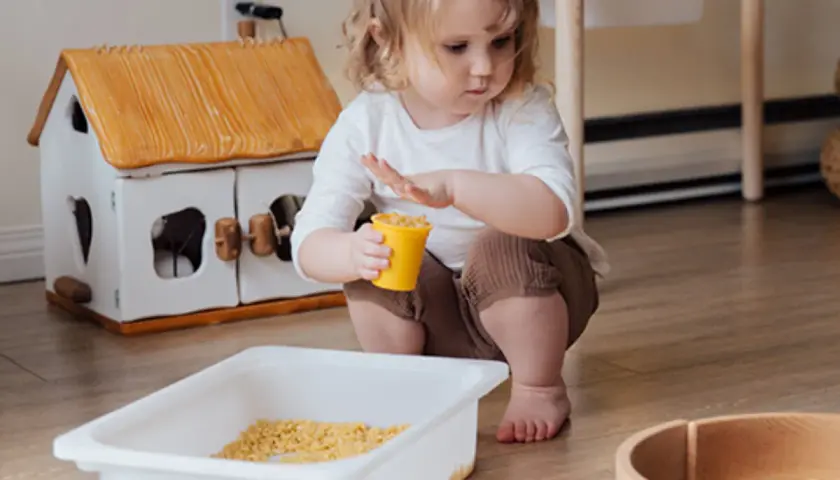 Bambina di 2 anni gioca con pasta in un vassoio, un'attività sensoriale divertente.
