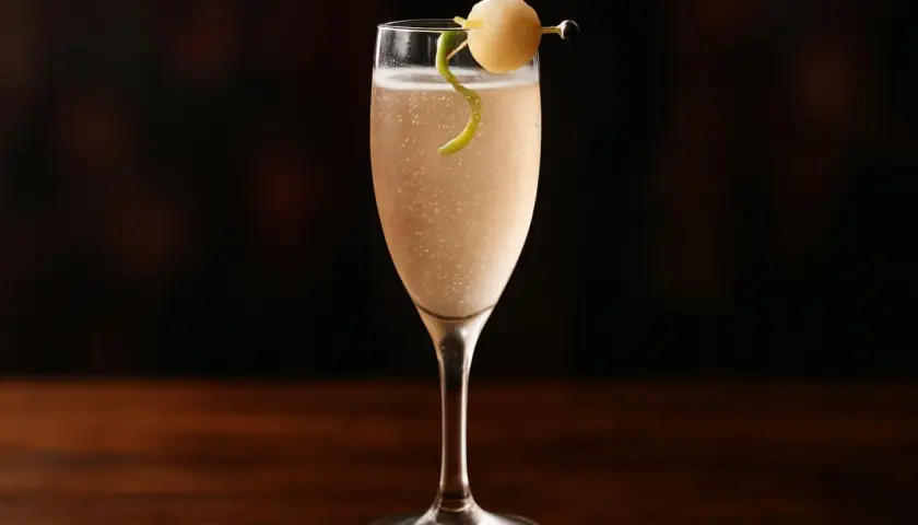Ett elegant drink med bubbel, garnerat med en citronskalsslinga och en rund fruktbit på en cocktailpinne.