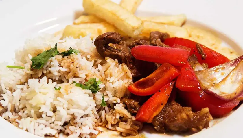 En tallrik med lomo saltado: ris, strimlat nötkött, rödlök, röd paprika och pommes frites.