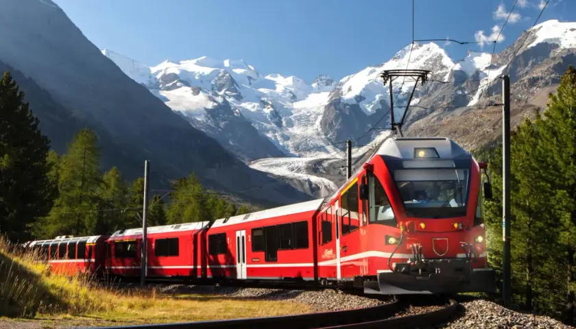Rött tåg i alpint landskap med snöklädda berg. En resa genom norra Italien med fantastisk utsikt.