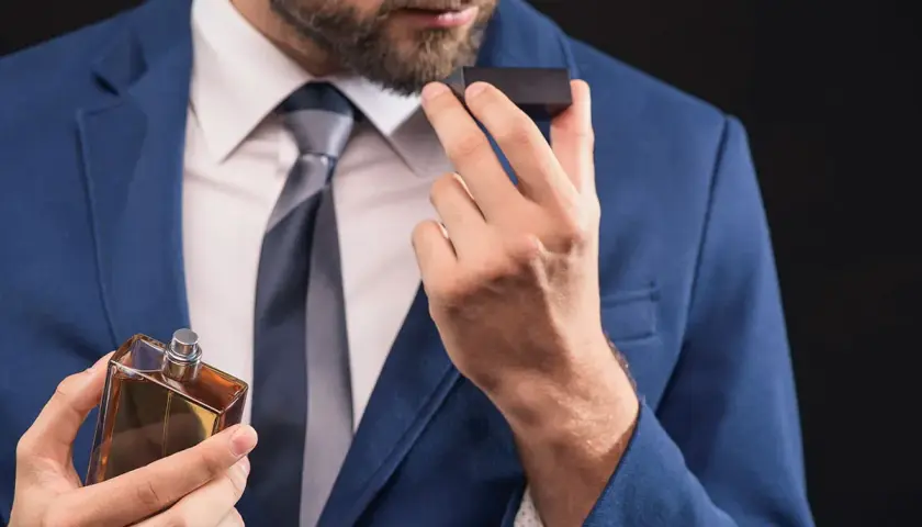 Mężczyzna w garniturze wącha perfumy z buteleczki.