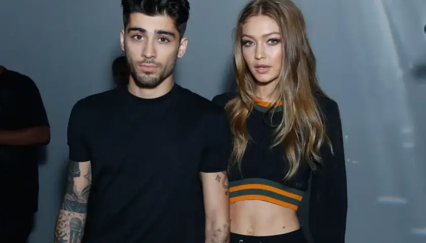Zayn Malik i Gigi Hadid pozują razem, oboje ubrani na czarno. Zayn ma tatuaże na ramionach, a Gigi odsłania brzuch w krótkim topie.