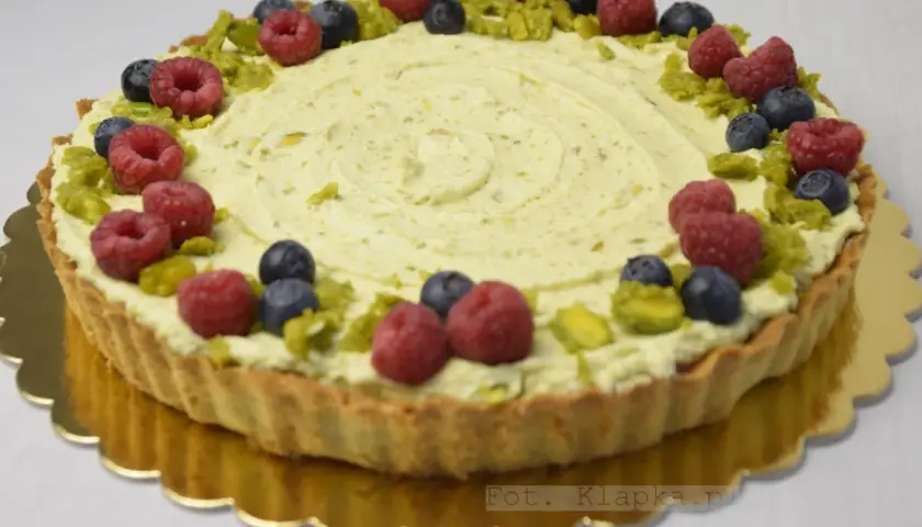 Tarta pistacjowa z białą czekoladą, ozdobiona malinami, borówkami i pistacjami.