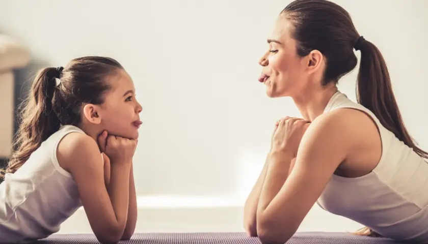 Mama i córka ćwiczą, wyciągając języki. Widać zaangażowanie mięśni wewnętrznych języka w zabawną zabawę.