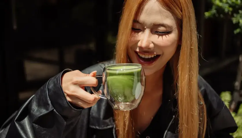 Lachende Frau hält eine Tasse Matcha. Mögliche matcha nebenwirkungen sind hier nicht sichtbar.