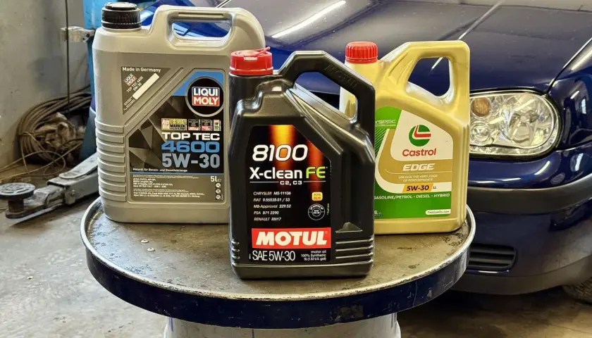 Trzy kanistry z olejem silnikowym: Liqui Moly, Motul i Castrol, na tle niebieskiego samochodu.