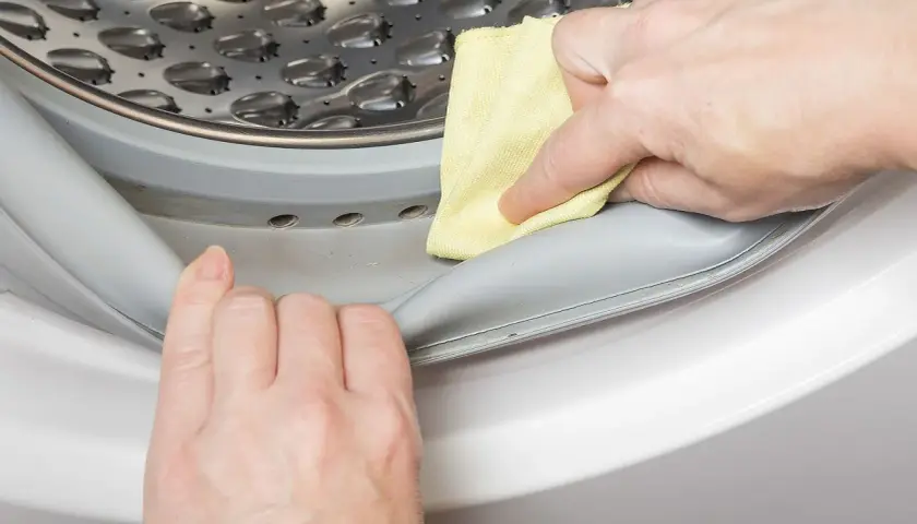 Manos limpian la goma de la lavadora con un paño amarillo para saber como quitar el mal olor de la lavadora.