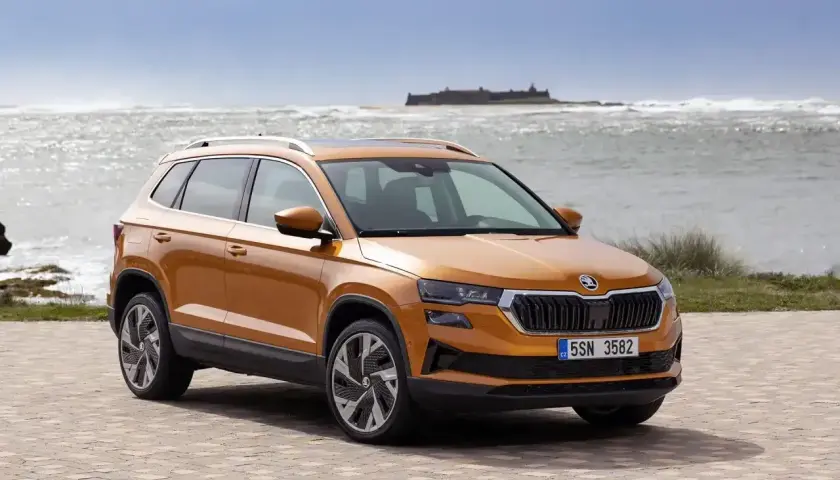 Pomarańczowa Skoda Karoq na tle morza. Sprawdź aktualny skoda cennik i wybierz swój wymarzony model.