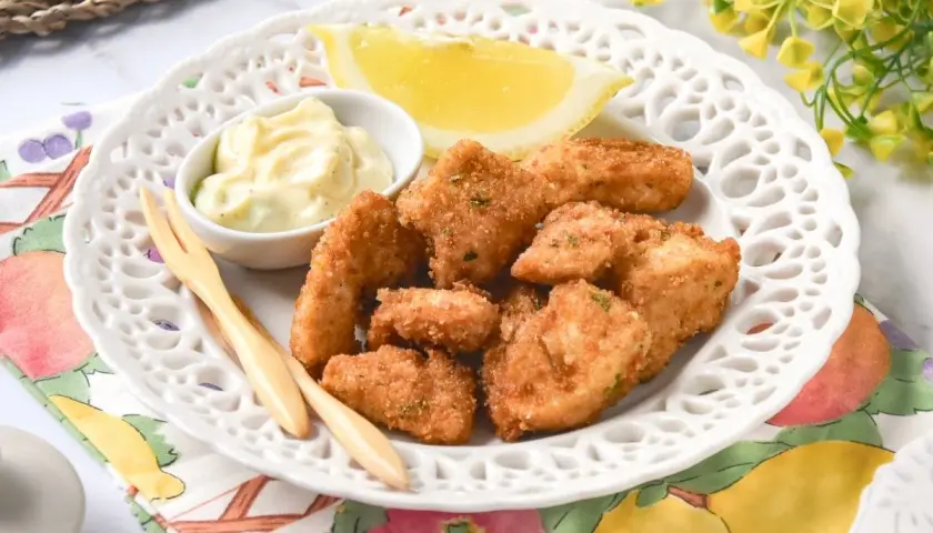 Deliciosas lagrimitas de pollo crujientes, servidas con mayonesa y limón en un plato blanco.